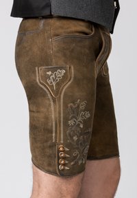 Bruna lädershorts med broderade blommönster och en ficka med dekorativ sömnad. Knappar på sidan ger en extra detalj.