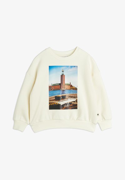 Cremfarbener Pullover mit lässiger Passform. Enthält ein zentrales Foto eines Backturms am Wasser, mit abgerundetem Saum und gerippten Bündchen.