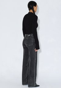 Schwarz gefärbte Jeans mit hohem Bund und lockerem Schnitt, vier Taschen und sichtbaren Nähte. Kombiniert mit einem eng anliegenden Langarmshirt.