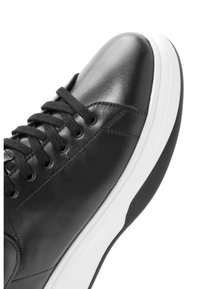 Sneaker in pelle nera con superficie liscia, punta rotonda, suola bianca e lacci neri. Presenta dettagli di cucitura lungo i lati.