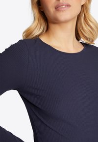 Top lungo a maniche lunghe blu navy con collo rotondo, caratterizzato da un tessuto testurizzato e una silhouette aderente, che enfatizza un design confortevole.