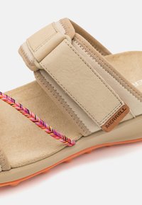 Beeži sandaal, mis on valmistatud suede materjalist, laia rihmaga, roosa ja lilla punutud detailiga ning tekstuuriga oranži tallaga. Omab Merrelli logo detaile.