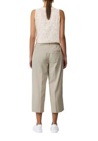 Beige cropped broeken met een getailleerde pasvorm en zijzakken, gecombineerd met een witte top zonder mouwen met een patroon. Gecombineerd met witte sneakers.