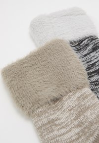 To sæt hyggelige sokker med en fluffy kant. Den ene er lysegrå med hvid, den anden er beige med sorte og hvide striber.
