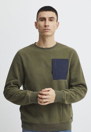 Olive green fleece sweatshirt with a navy blue chest pocket. Round neckline and ribbed cuffs, featuring a smooth texture and relaxed fit.