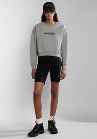 Grijze cropped sweatshirt met logo, zwarte fietsbroek, zwarte laarzen en een zwarte pet. Bevat stijlvolle zonnebril en enkellange witte sokken.