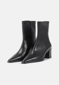 Stivali alla caviglia neri in pelle liscia con punta affusolata, zip laterale e tacco a blocco, caratterizzati da un design elegante e minimalista.