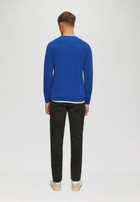 Blauer Pullover mit langen Ärmeln, Rundhalsausschnitt und taillierter Passform. Kombiniert mit schwarzen Jeans und hellen Sneakern. Einfarbiger Hintergrund.