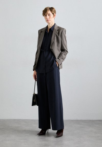 Grijze blazer over een marineblauw gestreept shirt en brede broekspijpen. Glanzende bordeauxrode hakken en een kleine zwarte handtas maken de look compleet.