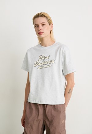 T-shirt en coton gris clair à manches courtes, arborant le logo "New Balance" en écriture marron sur la poitrine ; encolure arrondie, coupe décontractée.