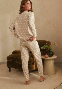 Beige pyjama set met een pompoenpatroon, gemaakt van zacht materiaal. Inclusief lange mouwen en aansluitende broeken met elastische boorden.