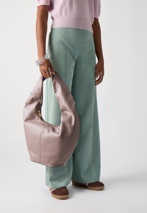 Sac hobo en cuir rose clair, avec une forme douce et une fermeture éclair. Pantalon en velours côtelé vert menthe et chaussures marron avec des accents blancs.