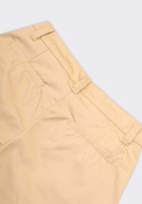 Pantaloni beige con una texture liscia, dotati di passanti per cintura, due tasche posteriori e un design sagomato, mostrati da un'angolazione dall'alto.