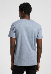 Maglietta grigia in heather, maniche corte, colletto a giro, tessuto morbido, vestibilità comoda, design semplice senza grafiche o motivi, indossata con pantaloni neri.