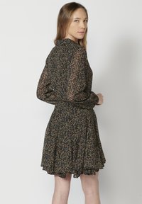 Abito nero a fiori con maniche lunghe in tessuto trasparente, vita stretta e gonna svasata. Presenta motivi floreali multicolori su uno sfondo scuro.