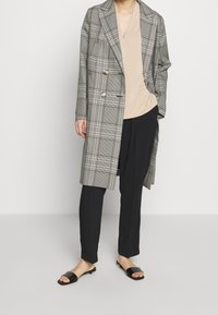 Grå och vit rutad dubbelknäppt kappa med breda slag, kombinerad med en beige topp och svarta skräddarsydda byxor. Svarta klacksandaler kompletterar looken.