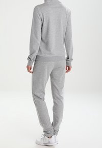 Sweat-shirt gris et joggers assortis en tissu doux. Le design comprend un col montant, des poignets côtelés et des ourlets aux chevilles.
