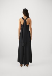 Rochie maxi neagră, fără mâneci, cu spate legat și deschis. Material neted, lungime până la podea, având un detaliu fluid care curge.