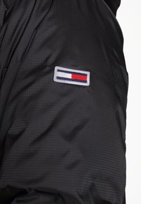 Giacca a vento nera con finitura testurizzata, dotata di una patch logo ricamata nei colori rosso, bianco e blu sul manica.