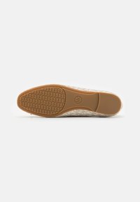 Semelle en caoutchouc marron d'une chaussure plate avec une prise avant texturée et un logo circulaire au centre, vue du dessous sur fond blanc.