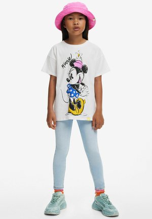 Vit t-shirt med en grafisk bild av en tecknad karaktär, blå prickig kjol, kombinerat med ljusa denimleggings och turkosa sneakers, rosa bucket hat.