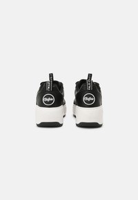 Baskets noires avec un col rembourré, une semelle blanche et une semelle extérieure en caoutchouc noir texturée. Elles comportent des écussons de logo et des languettes de maintien au talon.