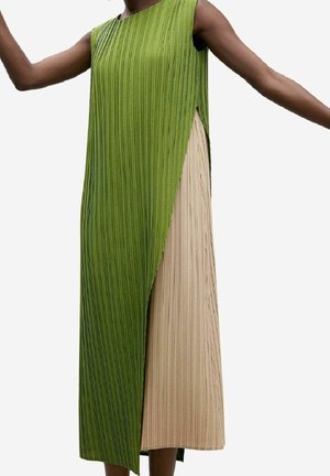 Robe longue sans manches avec plis verticaux, verte sur un côté recouvrant un tissu plissé beige, portée par un mannequin bras étendus.