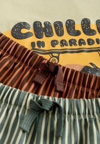 Deux paires de shorts à taille élastique rayés avec cordons de serrage sur un t-shirt jaune imprimé "Détente au paradis".