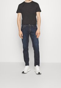 Czarny bawełniany t-shirt z krótkim rękawem, w połączeniu z ciemnoniebieskimi dżinsami i białymi trampkami z czarnymi akcentami. Prosty, codzienny strój.