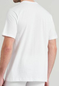 Man wearing plain white short-sleeve T-shirt shown from the back against a neutral background.