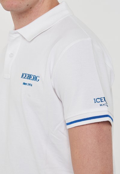 Polo shirt bianco a maniche corte realizzato in tessuto testurizzato. Presenta un logo ricamato blu "ICEBERG dal 1974" sul petto e accenti a righe sulle maniche.