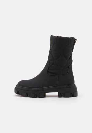 Botte noire mi-mollet avec dessus matelassé, semelle épaisse et robuste, et languette à l'arrière, conçue pour temps froid.