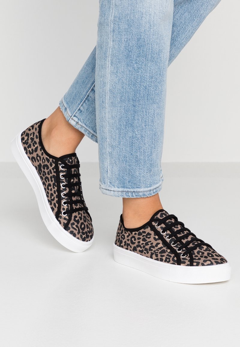 Leopard print canvas sneakers with black accents, white rubber sole, and six eyelets for laces, paired with light blue cropped jeans.