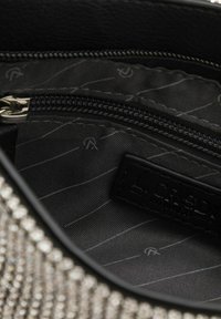 Interno della borsa con rivestimento in tessuto nero con sottili strisce diagonali, tasca con zip e etichetta del brand in rilievo su pelle.