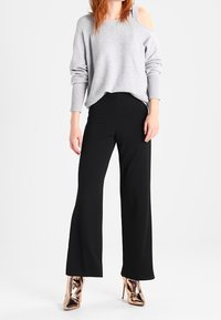 Grå stickad tröja med en öppen axeldesign, matchad med svarta vida byxor och glansiga brons högklackade skor.