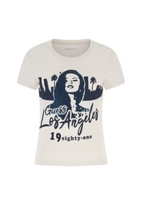 Krémové tričko s krátkymi rukávmi, na ktorom je námornícky grafický obrázok siluety ženy, text "Guess Los Angeles" a "1981."