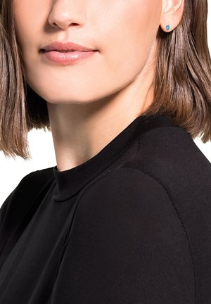 Top negro de cuello alto, con mangas cortas, textura suave y diseño ajustado. Los pendientes azules con studs añaden un toque de color contra la piel.