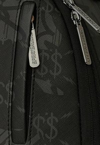 Mochila negra con una superficie texturizada, que presenta múltiples bolsillos con cremallera, herrajes plateados y detalles de patrón en la tela.