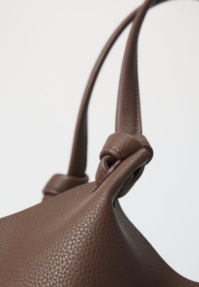 Gros plan sur une sangle de sac à main en cuir marron texturé nouée contre un fond clair.