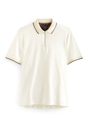 Polo blanc à manches courtes avec des rayures verticales subtiles, col beige et poignets bordés de noir, et une fermeture zippée à l'avant.
