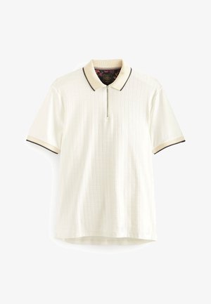 Polo blanc à manches courtes avec des rayures verticales subtiles, col beige et poignets bordés de noir, et une fermeture zippée à l'avant.