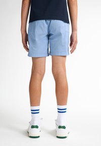 Ljusblå shorts med upprullade fållar, bärs med vita sneakers med gröna och gula detaljer, samt vita strumpor med blå ränder.