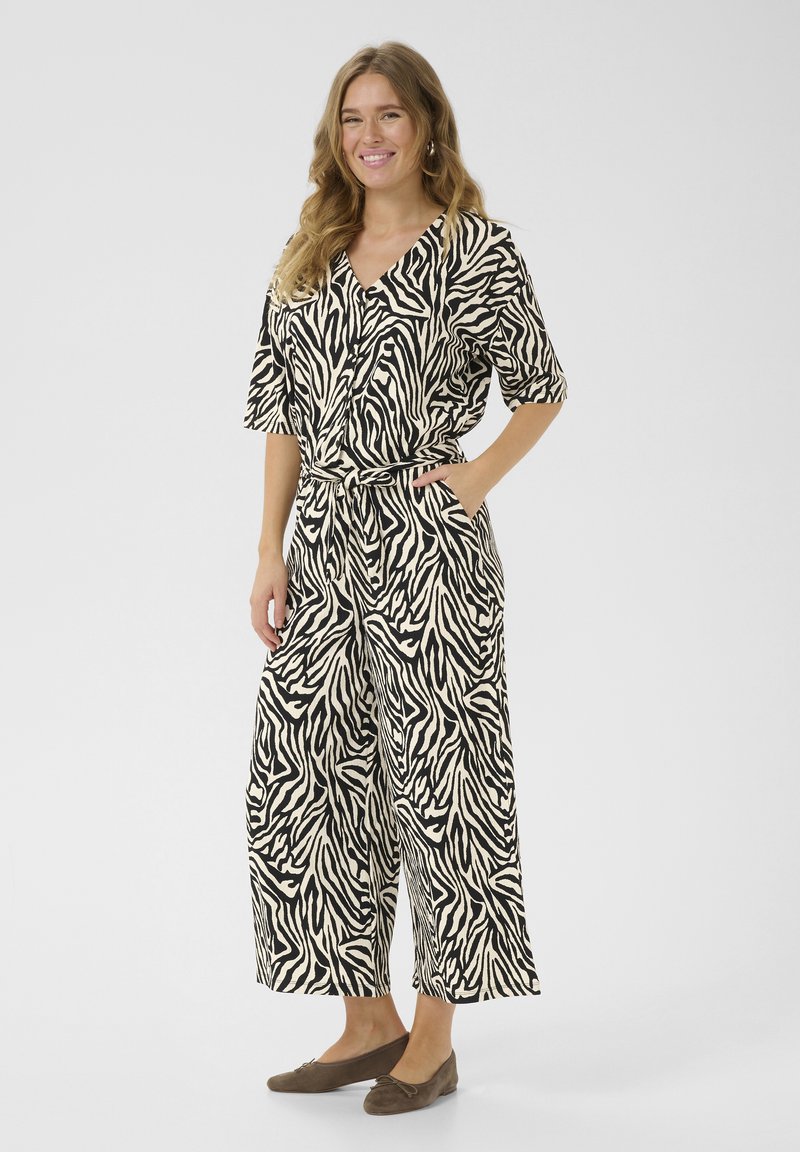 Black and white zebra-patterned jumpsuit with short sleeves, a tie waist, and wide legs; made from lightweight fabric.
