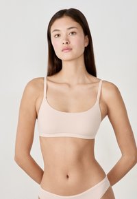 Bra wireless rosa chiaro con scollatura rotonda, sottili bretelle regolabili e texture liscia, progettato per comfort e facilità d'uso.