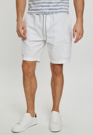 Hvide linned cargo shorts med elastisk talje, snor og sidelommer, parret med hvide sneakers på en neutral baggrund.