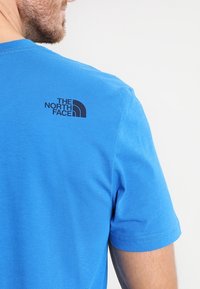 Blå bomullst-shirt med korta ärmar, rund halsringning och en svart logotyp för "The North Face" på övre delen av ryggen.
