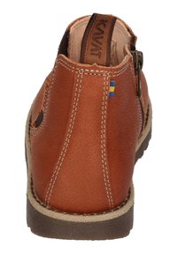 Brown leather shoe with a textured finish, featuring contrasting stitching, a back zipper, and a decorative logo tag with a small flag accent.