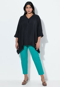Tunic nera fluente con scollatura a V e maniche a tre quarti abbinata a pantaloni teal sartoriali. L'outfit presenta un leggero orlo asimmetrico.