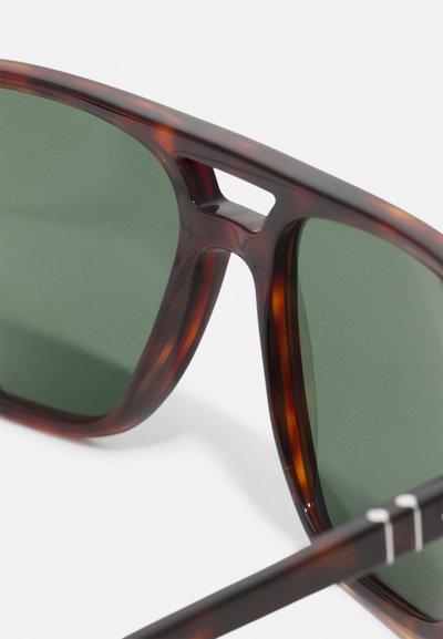 Braun gefleckte Sonnenbrille mit grünen Gläsern, die über ein einzigartiges Ausschnittdesign an der Brücke und eine schlanke, rechteckige Form verfügt.