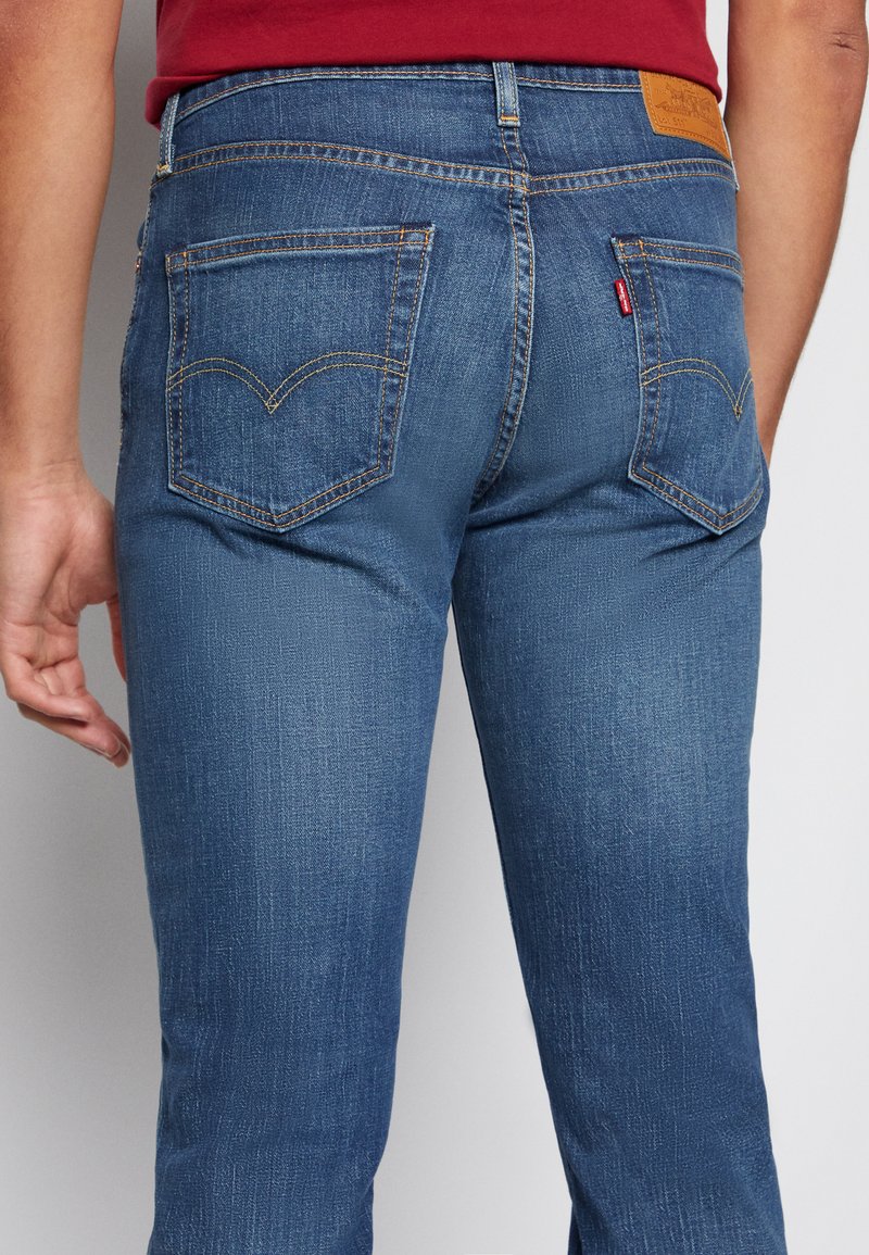 Mörkblå denimjeans med raka ben, fem fickor och distinkt gul söm. Har en läderlapp på den bakre midjan.
